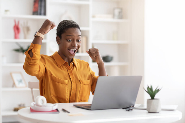 Emocional mujer de negocios afroamericana celebrando el éxito, trabajando en el ordenador portátil - Foto, Imagen