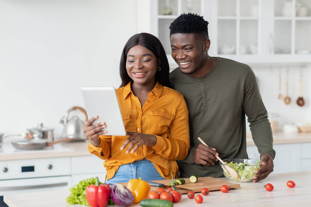 Cônjuges afro-americanos felizes preparando alimentos na cozinha e usando tablet digital - Foto, Imagem