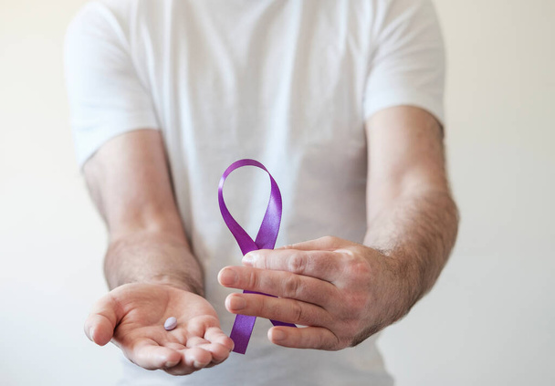 Manos masculinas sosteniendo cinta púrpura y píldora púrpura. Epilepsia, cáncer de páncreas y símbolo de Alzheimer. - Foto, imagen