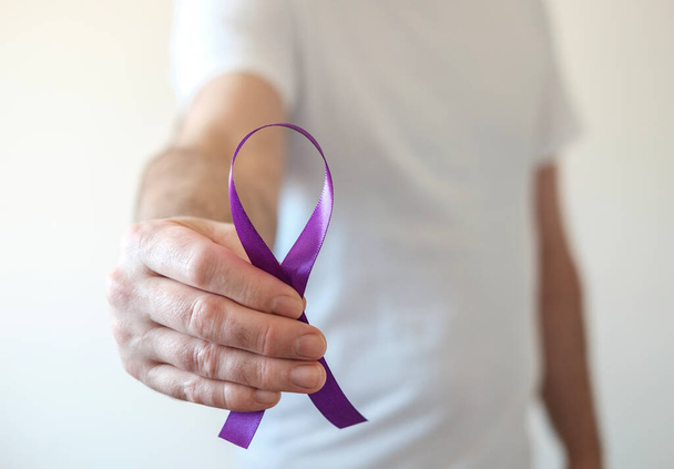 Een mannelijke hand houdt een paars lint vast. Epilepsie, alvleesklierkanker en Alzheimer symbool. - Foto, afbeelding