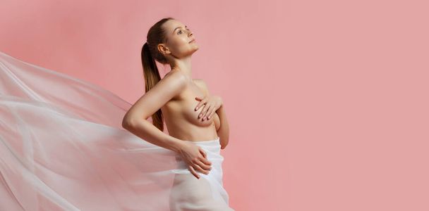 Cropped female body in light underwear covered with milky colored silk fabrik isolated over pink studio background. - Foto, immagini