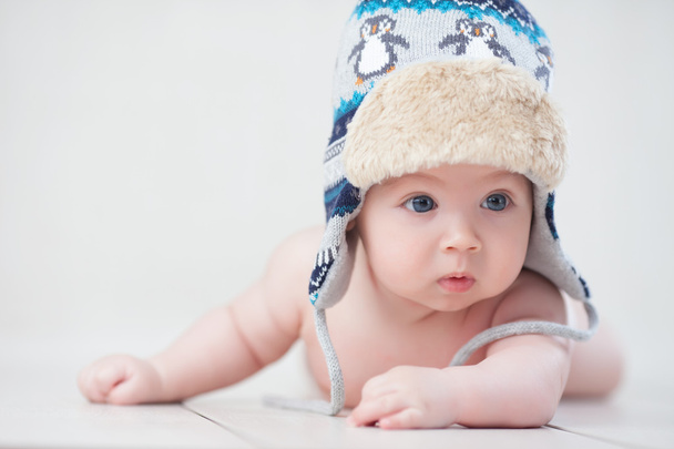 Baby in winter hat lying on the floor - Фото, изображение
