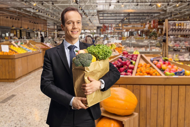 Bussinesman holding a paper bag with groceries inside a grocery store - Foto, Bild