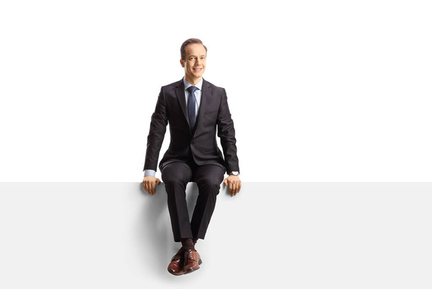 Professional man in suit and tie sitting on a blank panel isolted on white background - Photo, image