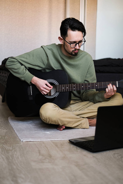 Adam dizüstü bilgisayardan gitar çalmayı öğreniyor. - Fotoğraf, Görsel