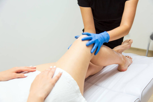 Professional sugarist preparing the client for a procedure, spreading the gel on her long slim legs - Foto, afbeelding
