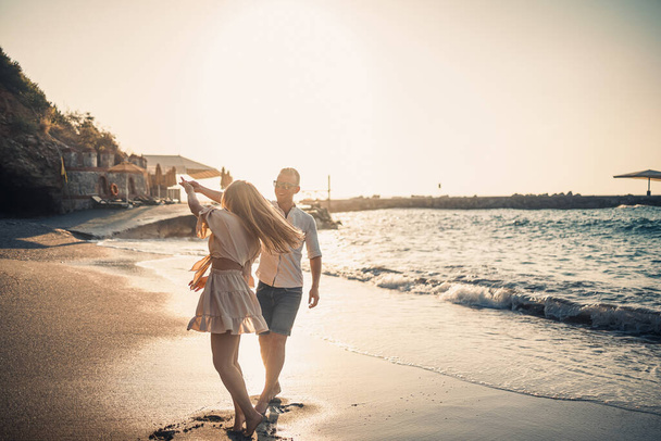 Un couple amoureux se promène sur la plage près de la mer. Jeune famille au coucher du soleil au bord de la mer Méditerranée. Concept vacances d'été - Photo, image
