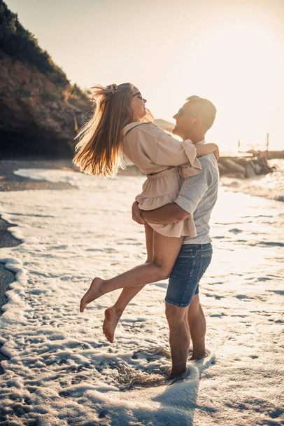 Una pareja enamorada está caminando por la playa cerca del mar. Joven familia al atardecer junto al mar Mediterráneo. Concepto vacaciones de verano - Foto, Imagen