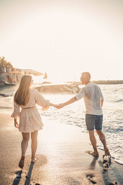 Zakochana para spaceruje po plaży w pobliżu morza. Młoda rodzina o zachodzie słońca nad Morzem Śródziemnym. Koncepcja wakacji letnich - Zdjęcie, obraz