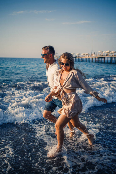 ρομαντικό νεαρό ζευγάρι ερωτευμένο μαζί στην άμμο περπατά κατά μήκος της παραλίας της Μεσογείου. Καλοκαιρινές διακοπές σε μια ζεστή χώρα. - Φωτογραφία, εικόνα