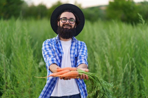 Sonriente hombre sosteniendo un montón de zanahorias en sus manos - Foto, Imagen