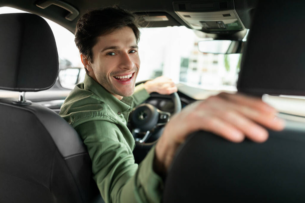Веселий молодий чоловік керує новим автомобілем після покупки, сидячи на водійському сидінні автомобіля в дилерському центрі
 - Фото, зображення