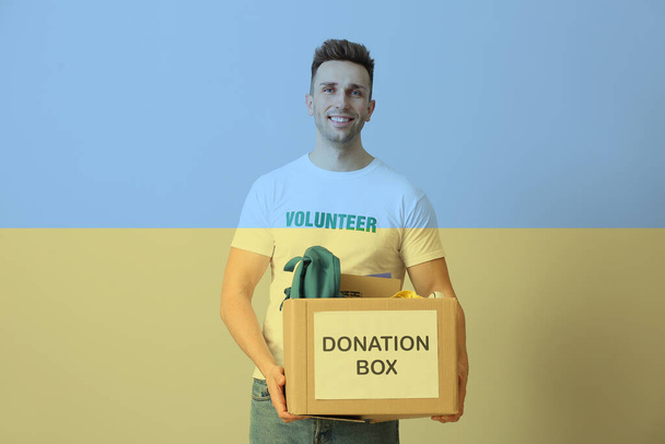 Doble exposición del voluntario masculino con caja de donación y bandera de Ucrania. Ayuda humanitaria a los refugiados - Foto, Imagen