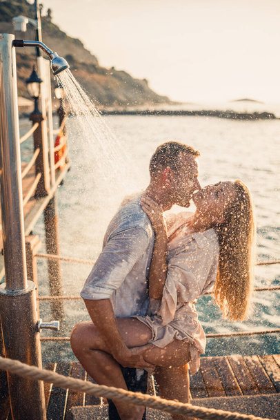 Deniz kenarında mutlu bir çift. Bir adam ve bir kız açık hava rıhtımında duşun altındalar. Tatildeki mutlu çift. Deniz kenarındaki kadın ve erkek. - Fotoğraf, Görsel