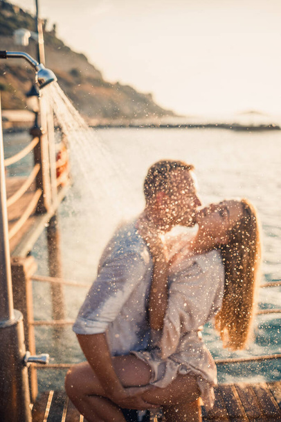 Glückliches Paar am Meer. Ein Mann und ein Mädchen stehen unter der Dusche auf einem Freiluftsteg. Glückliches Paar im Urlaub. Mann und Frau am Meer. Selektiver Fokus - Foto, Bild