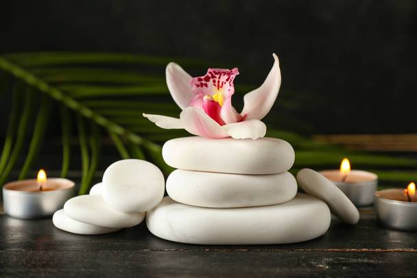 Spa stones with orchid flower and aroma candles on dark wooden background - Photo, Image