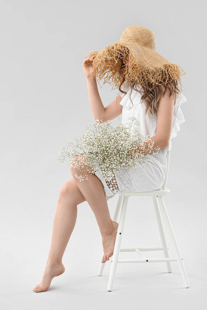 Pretty young woman with bouquet of flowers sitting on chair against light background - Fotó, kép