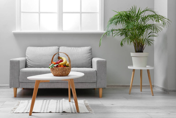 Interior of light living room with grey sofa, wooden table and fruit basket - 写真・画像