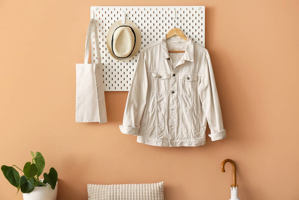 Pegboard with shopping bag, hat and jacket hanging on beige wall - Photo, Image