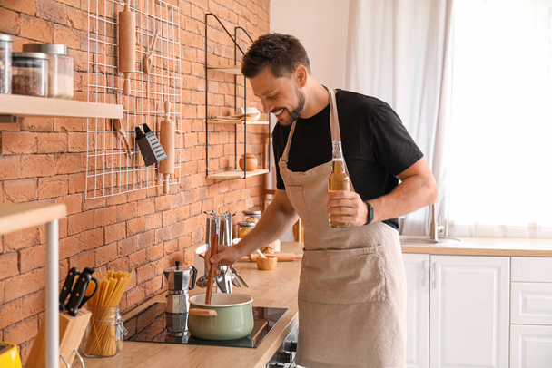 Handsome man drinking beer while cooking in kitchen - Fotoğraf, Görsel