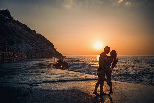Beau couple amoureux sur fond de coucher de soleil au bord de la mer. Jeune femme et homme embrasser par la mer au coucher du soleil - Photo, image