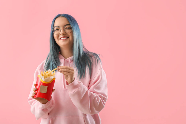 Mujer joven con pelo inusual y paquete de papas fritas en el fondo de color - Foto, imagen