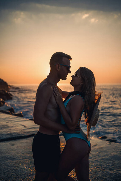 Prachtig verliefd stel op de achtergrond van de zonsondergang aan zee. jonge vrouw en man knuffelen door de zee bij zonsondergang - Foto, afbeelding