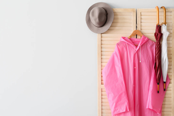 Klappleinwand mit rosa Regenmantel, Regenschirmen und Hut in der Nähe der Lichtwand - Foto, Bild