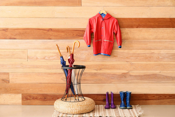 Soporte con paraguas, botas de goma y impermeable rojo para niños colgando de la pared de madera - Foto, imagen
