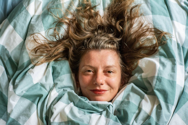 šťastný uvolněný ženský portrét spící v peřině. dívka leží v posteli horní pohled - Fotografie, Obrázek