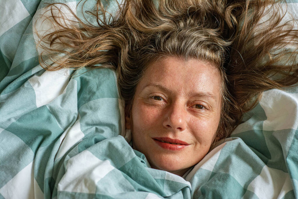 Χαρούμενη χαλαρή γυναίκα πορτρέτο κοιμάται σε πάπλωμα. κορίτσι βρίσκεται στο κρεβάτι πάνω όψη - Φωτογραφία, εικόνα