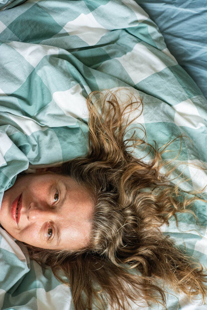 happy relaxed woman portrait sleeping in duvet. girl lies in bed top view - Fotografie, Obrázek