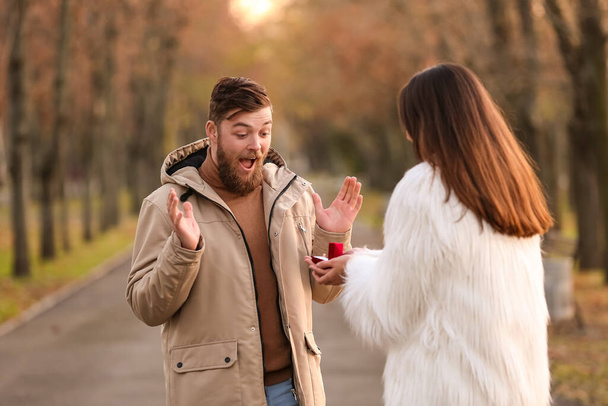 Junge Frau macht ihrem überraschten Freund im Park einen Heiratsantrag - Foto, Bild