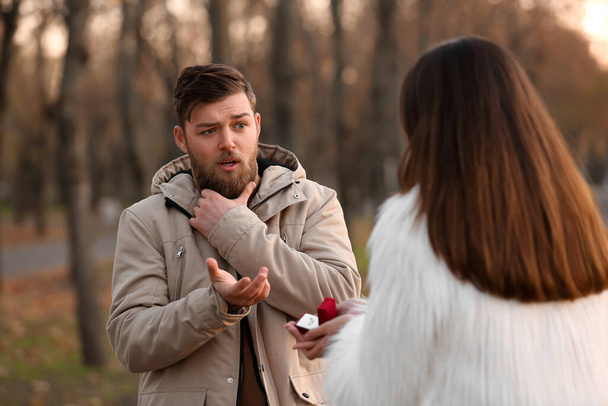 Young woman proposing to her shocked boyfriend in park - 写真・画像