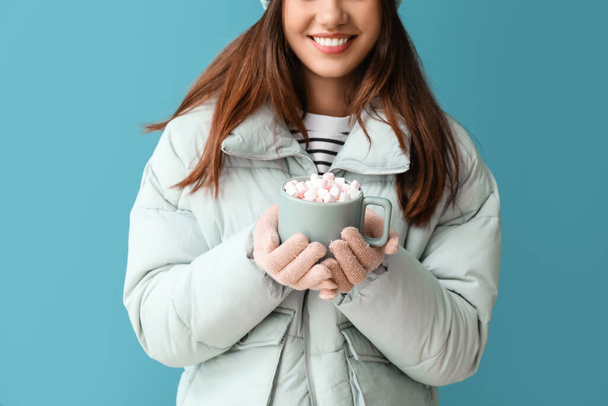 Young woman in warm gloves with cup of cocoa on blue background - Fotó, kép