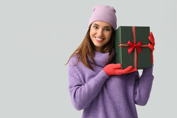 Junge Frau in roten Handschuhen mit Geschenkschachtel auf hellem Hintergrund - Foto, Bild