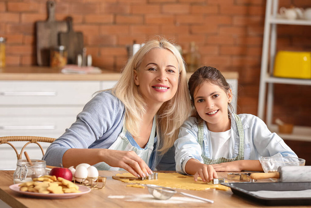 Kislány a nagyanyjával, tésztát vág sütikért a konyhában. - Fotó, kép