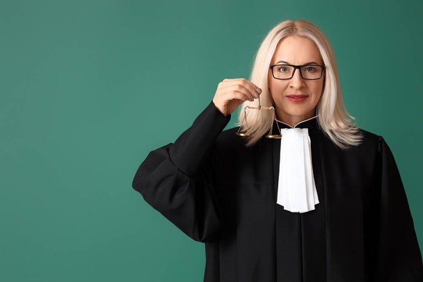 Érett női bíró köntösben igazságszolgáltatási mérleggel zöld alapon - Fotó, kép