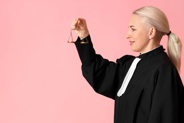 Ώριμη γυναίκα δικαστής με ρόμπα με ζυγαριές δικαιοσύνης σε ροζ φόντο - Φωτογραφία, εικόνα