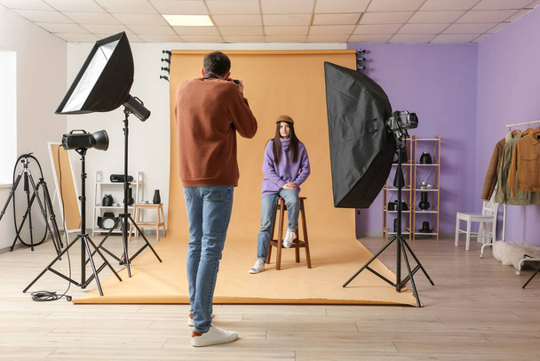 Fotógrafo do sexo masculino tirando foto de uma jovem sentada em um banquinho no estúdio - Foto, Imagem