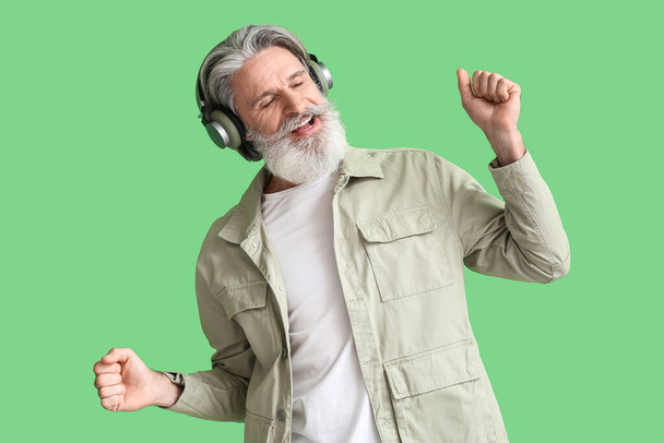 Senior man in headphones listening to music on green background - Photo, Image