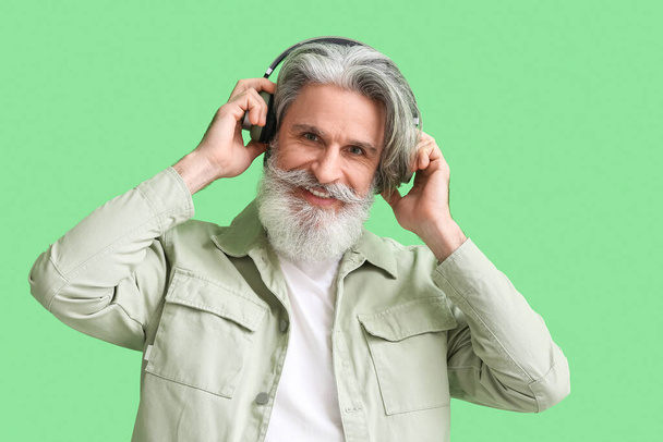 Senior man in headphones on green background - Fotoğraf, Görsel