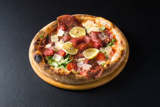 pizza met varkensvlees, tomaten, kaasvlokken, salade en citroenschijfjes - Foto, afbeelding