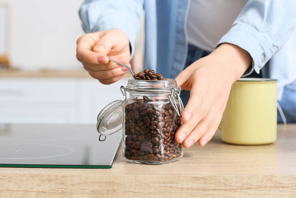 Young woman taking coffee beans from jar on counter in kitchen, closeup - Photo, Image