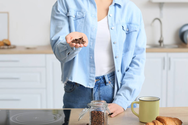 Giovane donna con chicchi di caffè vicino al bancone in cucina - Foto, immagini