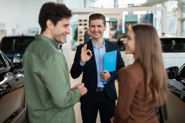 Auto showroom manager showing okay gesture to happy young customers at car dealership - Photo, Image