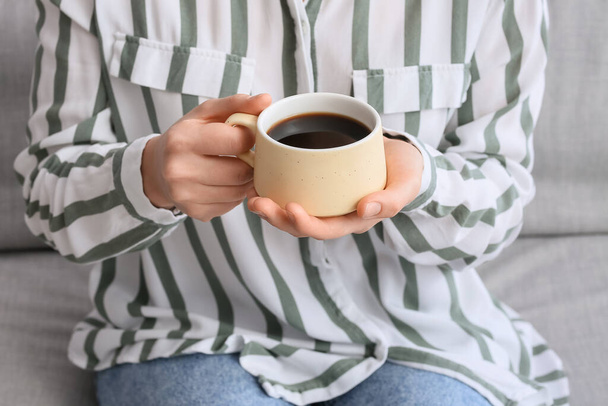 Young woman with cup of tasty coffee sitting on sofa in kitchen, closeup - Fotó, kép