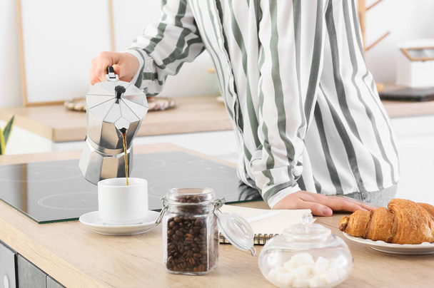 Junge Frau schüttet Kaffee in Tasse in Küche - Foto, Bild