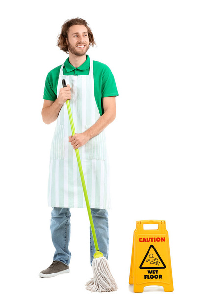 Νέος εργαζόμενος της υπηρεσίας καθαρισμού με σφουγγαρίστρα και πινακίδα προσοχή σε λευκό φόντο - Φωτογραφία, εικόνα