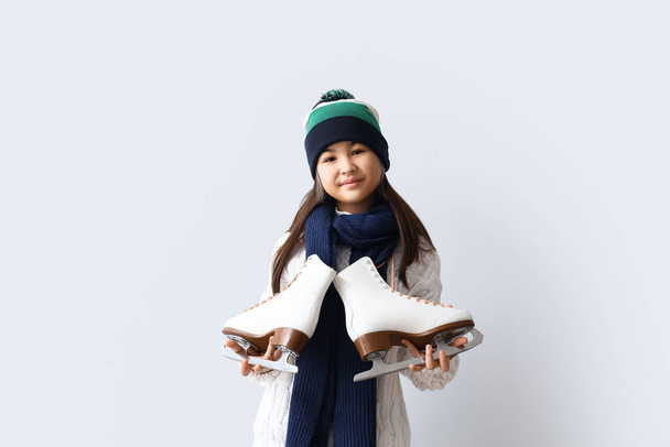 Pieni aasialainen tyttö lämpimissä vaatteissa luistimet kevyellä taustalla - Valokuva, kuva